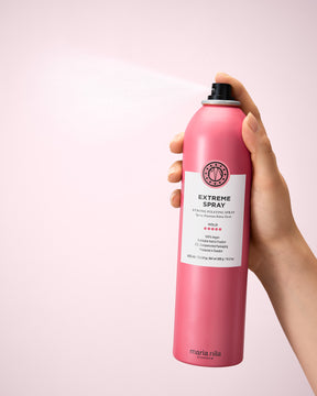 Hand holding  a bottle of Extreme Spray against a light pink background
