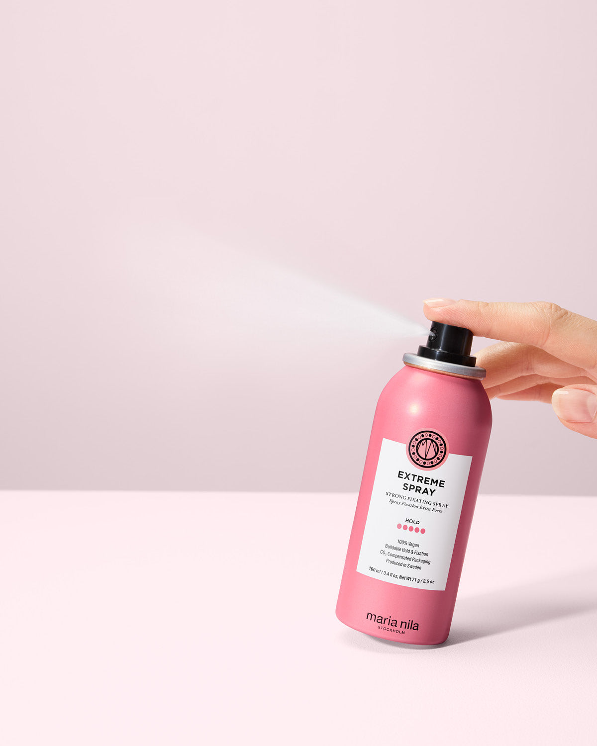 Extreme Spray bottle held by a hand on a light pink background