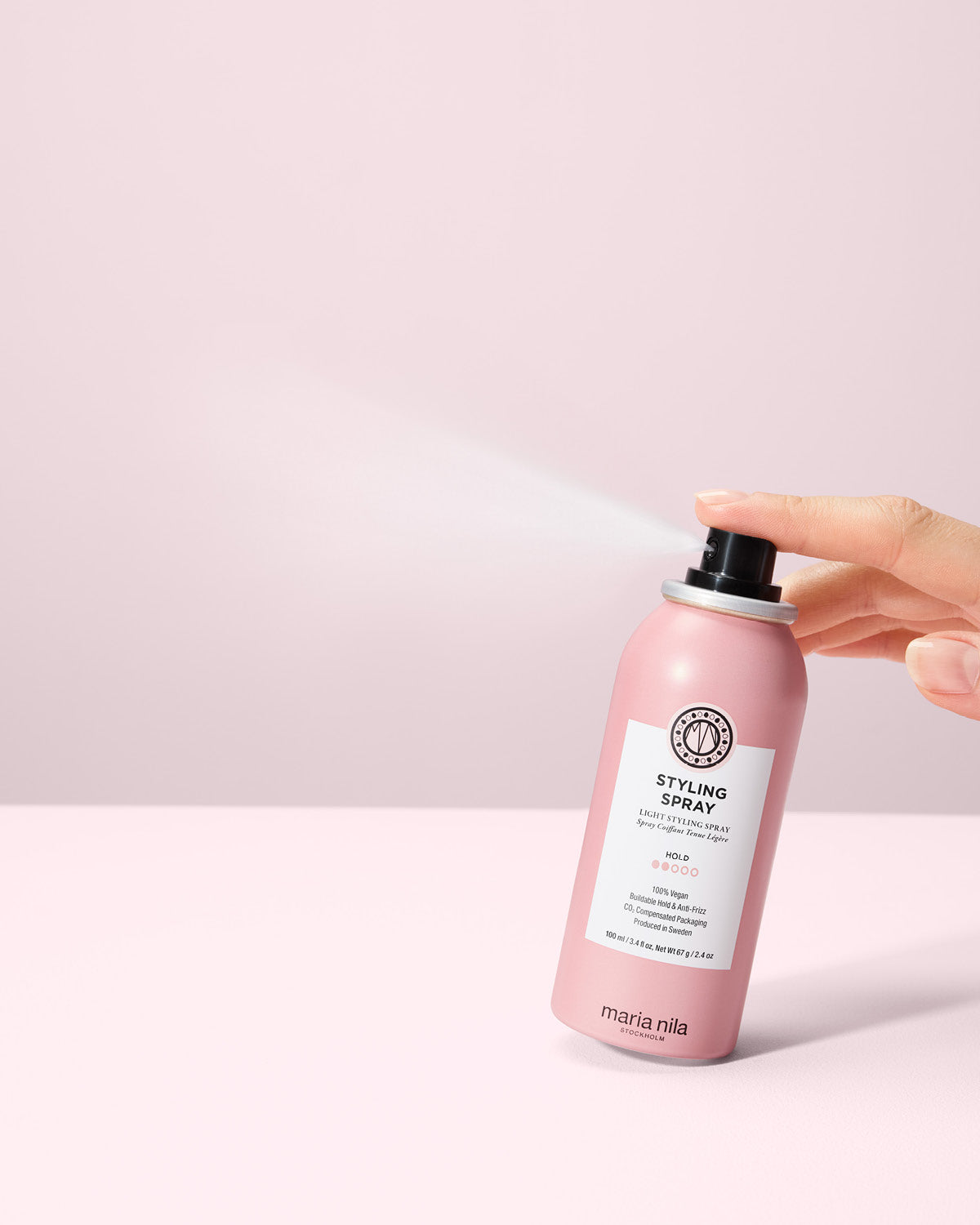 Small Styling Spray bottle held by a hand on a light pink background