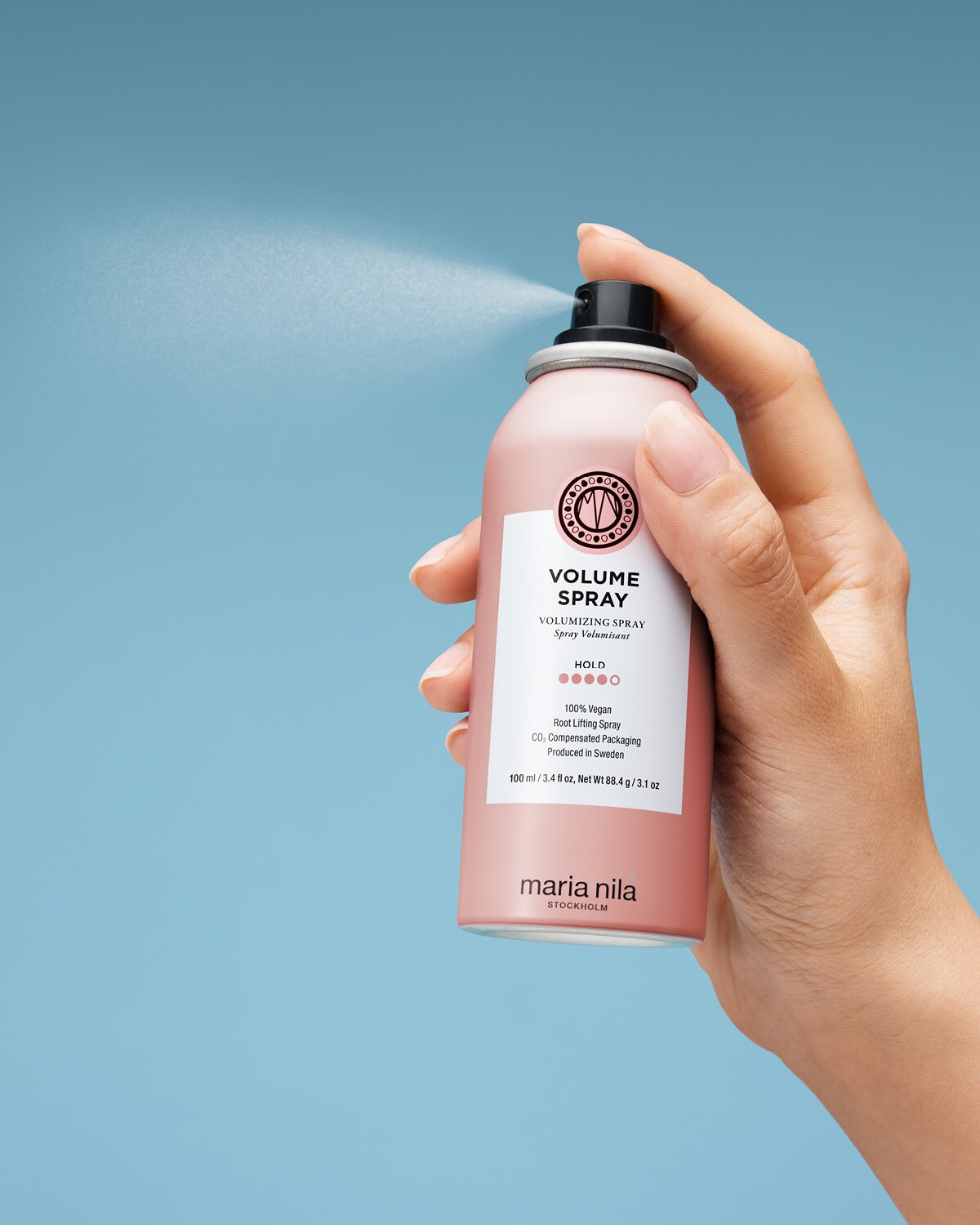 Hand holding a pink Maria Nila Volume Spray can against a light blue background