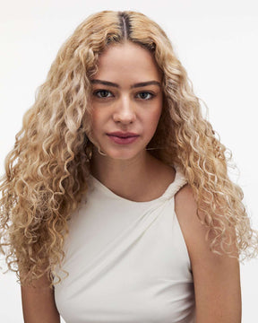 Woman with curly blonde hair wearing a white top on a white background