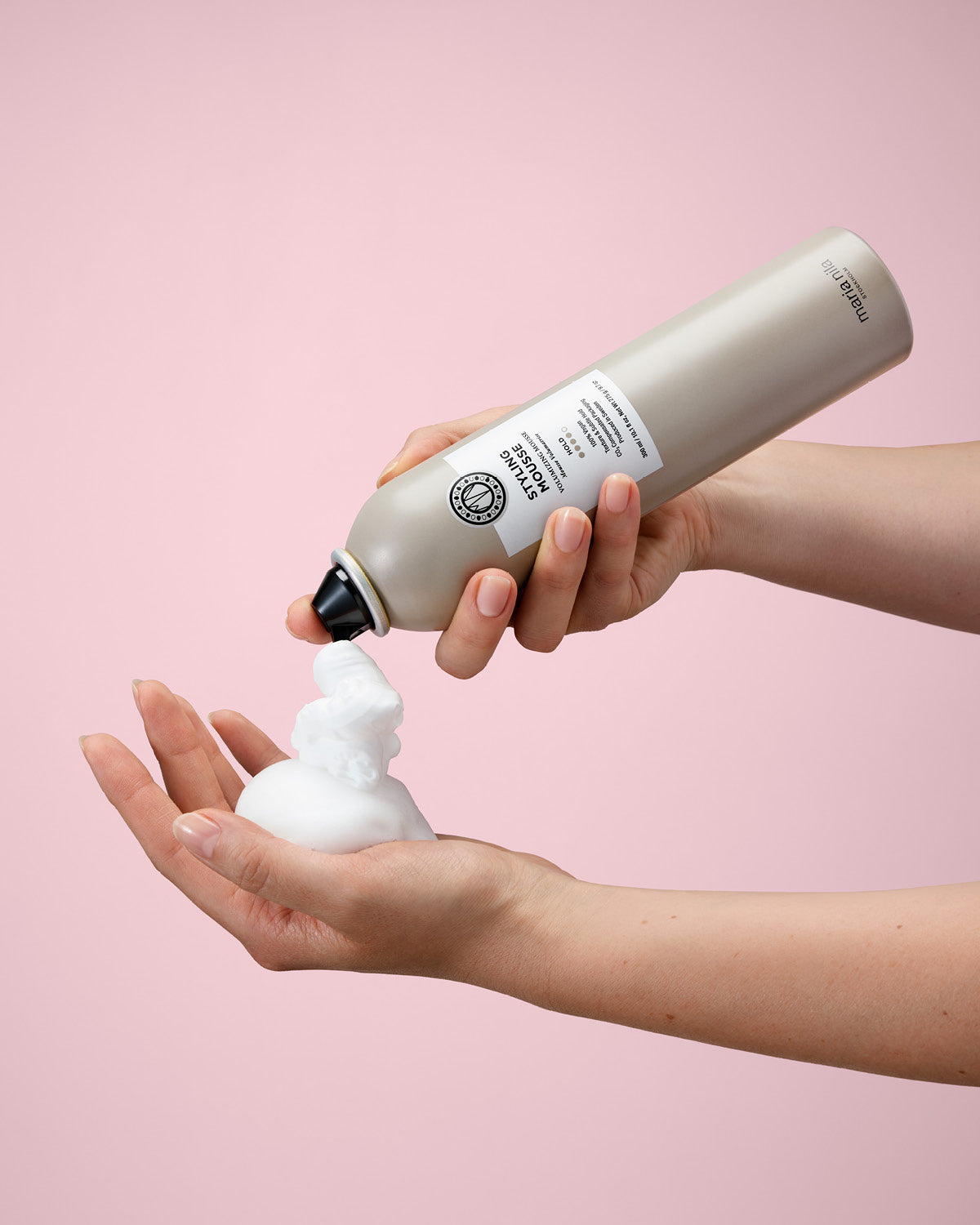 Person holding a bottle of Styling Mousse and pouring it onto their hand against a pink background
