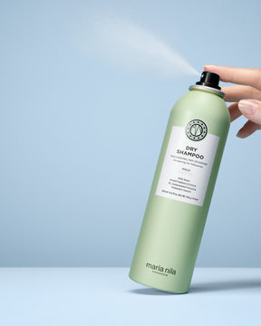Green bottle of Maria Nila dry shampoo being sprayed on a light blue background