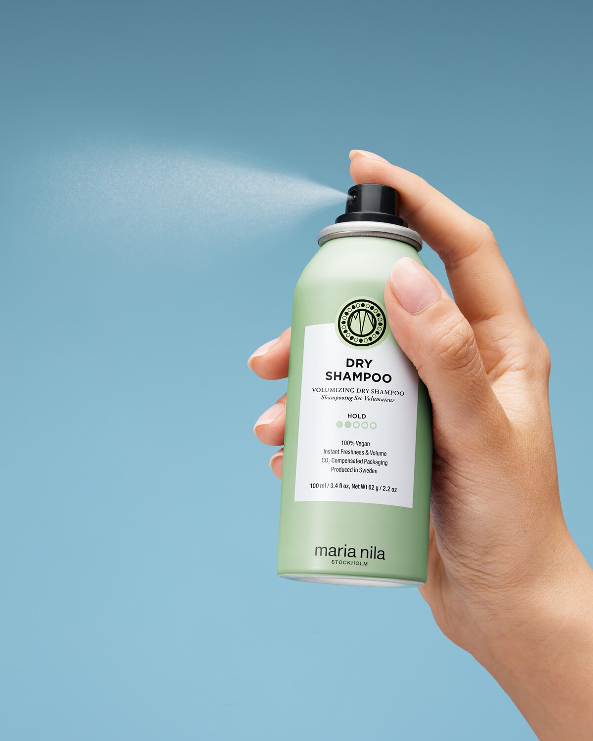 Hand holding a green Maria Nila dry shampoo can against a light blue background