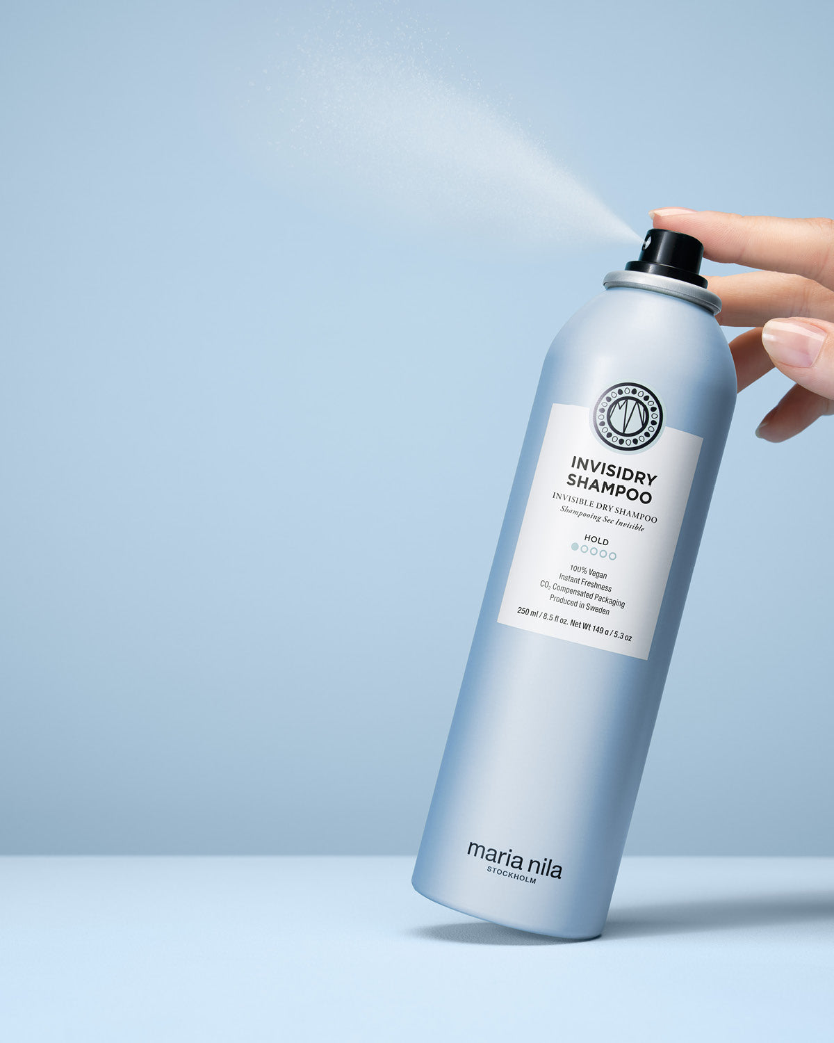 Invisidry Shampoo bottle being sprayed with a hand on a light blue background