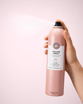 Hand holding a pink Volume Spray can against a light pink background