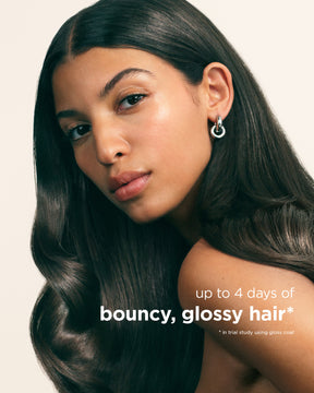 Woman with long, smooth, glossy dark hair and silver hoop earrings against a neutral background.