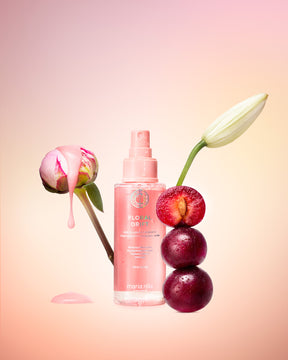Pink bottle of Maria Nila Floral Drift hair mist with flowers and plums on a gradient background